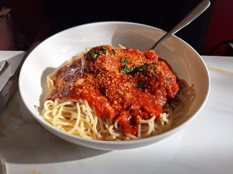 Spaghetti with meatballs, red sauce, parmesan cheese, and parsley in a white bowl.
