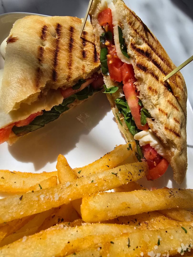 Grilled panini sandwich with tomatoes, mozzarella, and basil, served with seasoned french fries.