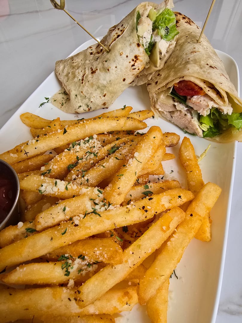 Two chicken wraps with lettuce, tomatoes, and cheese, served with a side of seasoned french fries.