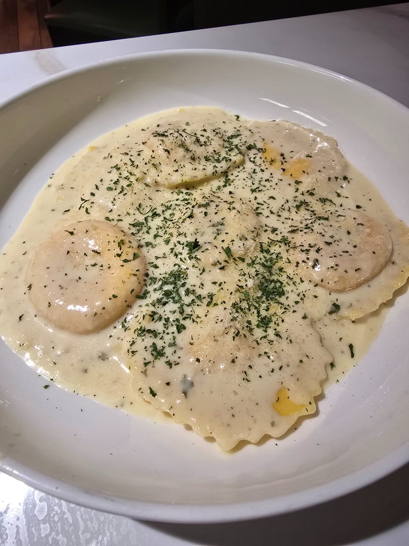 Ravioli pasta in a creamy white sauce, garnished with parsley and grated cheese.